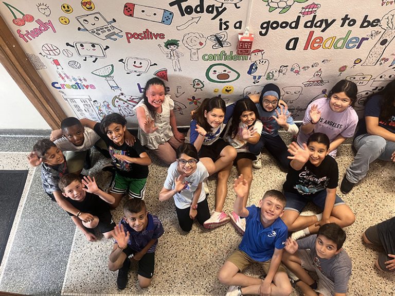 Students in the 2024 Summer Discovery Program at Lindbergh Elementary pose in front of a mural they are creating.